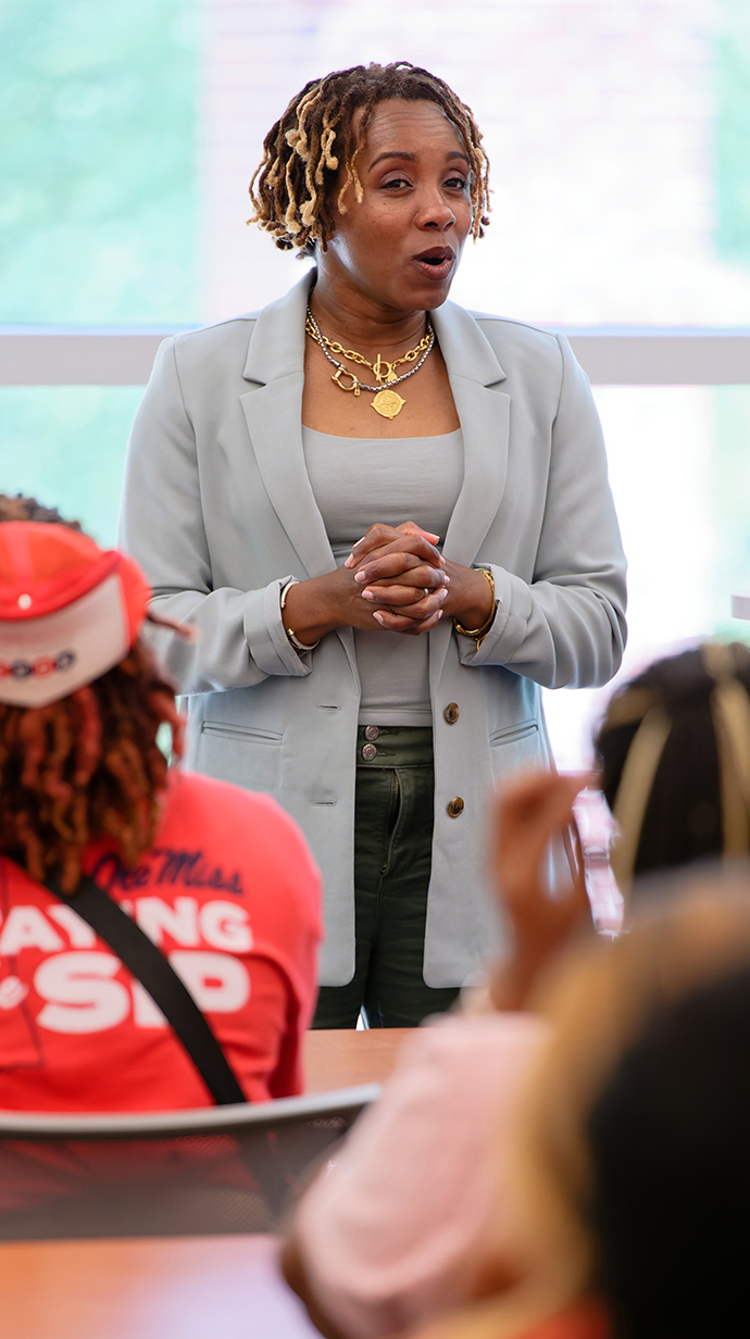 A woman talks at the front of a classroom full of young people.