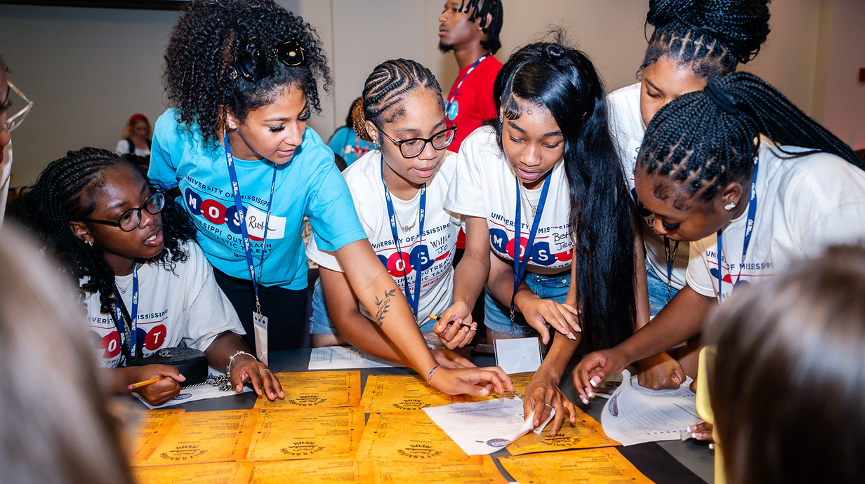 Several young women examine paperwork around a table for a team-building exercise.