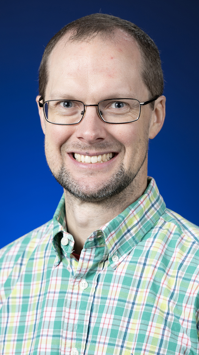 Headshot of a man wearing glasses and a green plaid shirt,