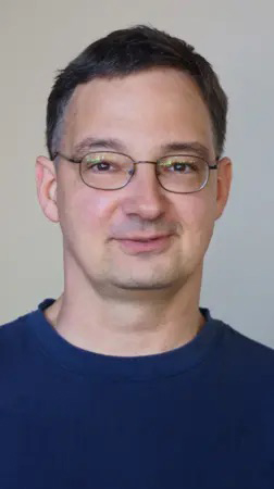 Headshot of a man wearing glasses and a dark blue T-shirt.
