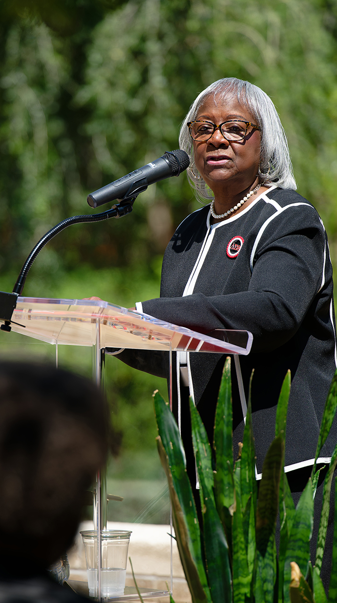A woman speaks into a microphone on an outdoor lectern.