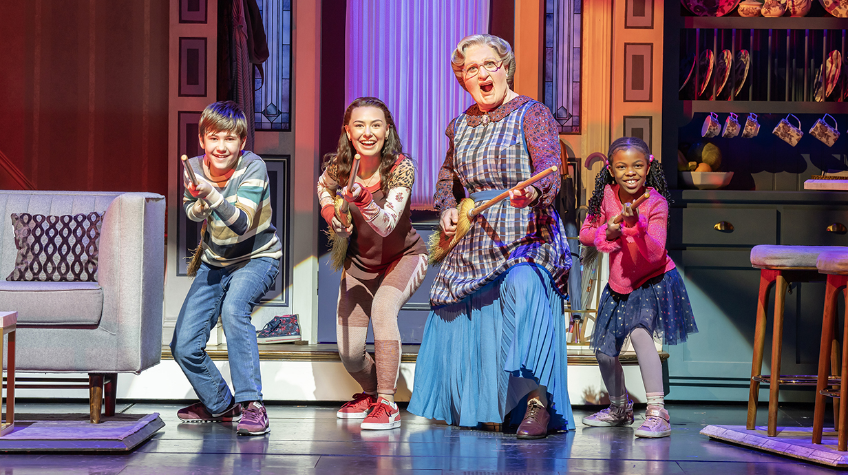 A man dressed as a woman and three children sing and dance onstage.