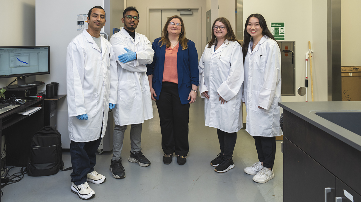 A woman stands with four young people, all wearing white lab coats, in a laboratory.