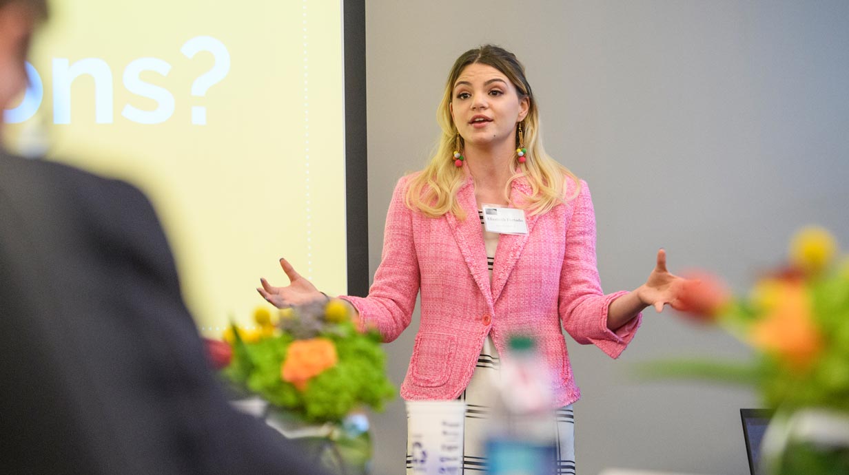 Female student in a pink jacket giving a presentation. 