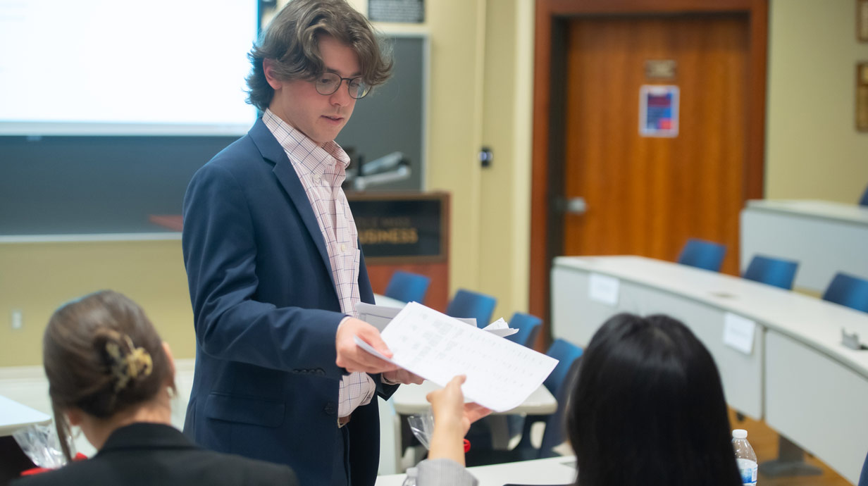 Male student handing a female student a paper. 