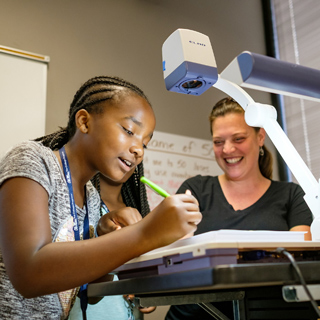 A teacher and student complete a math problem on a projector screen.