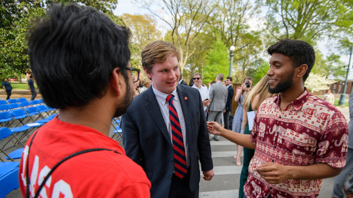 Three members of the Ole Miss Associated Student Body fraternize in The Circle on a sunny day.