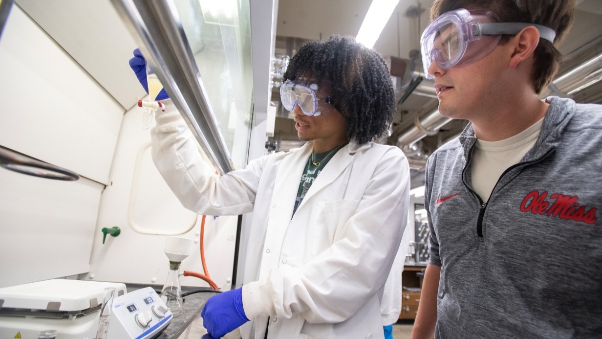 Students work together to in a chemistry lab under a fume hood