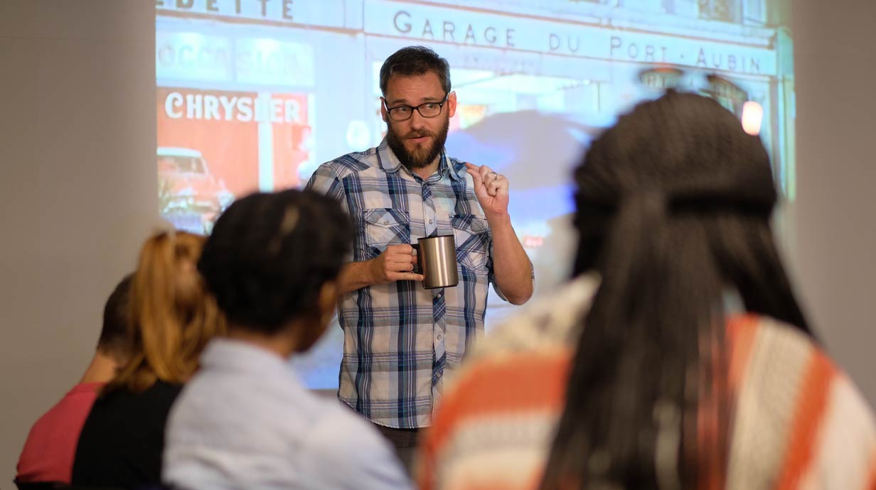 Professor discussing a film with students. Colorful still of film in background.