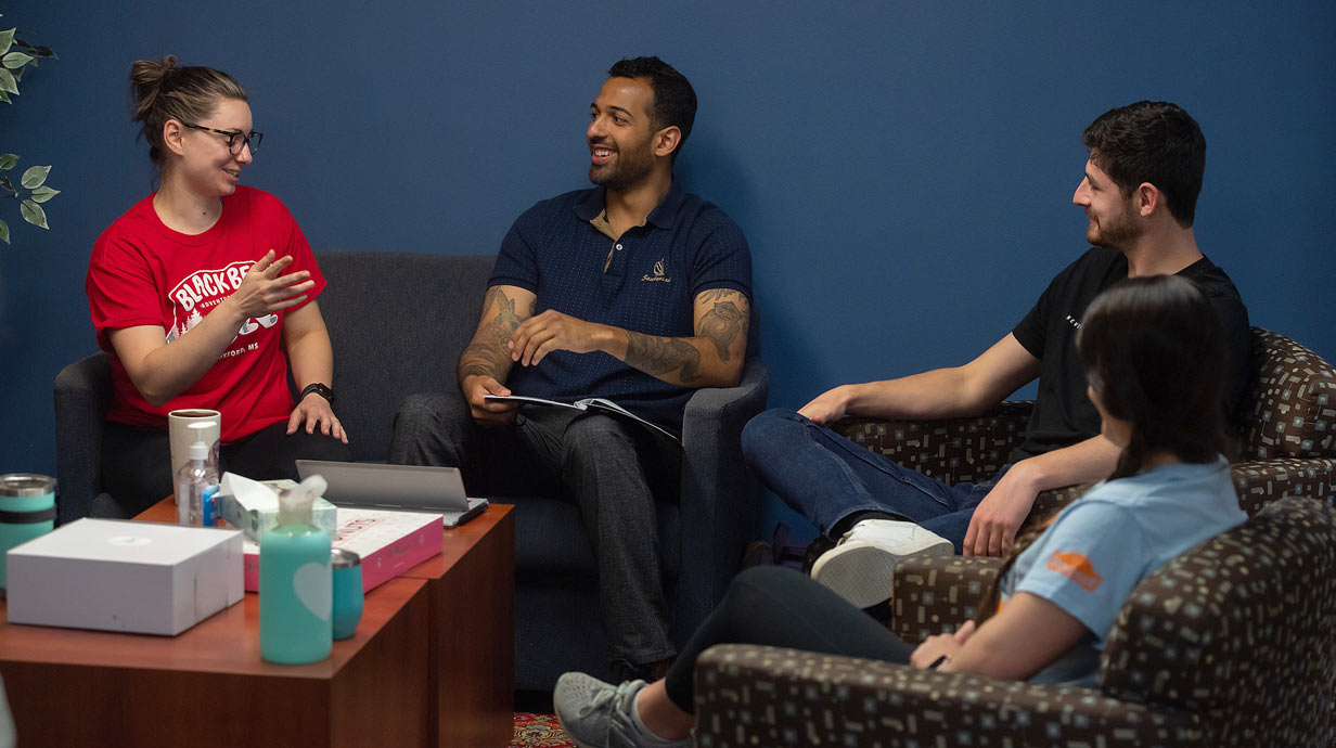 Four students sitting on a couch and chair having a discussion.