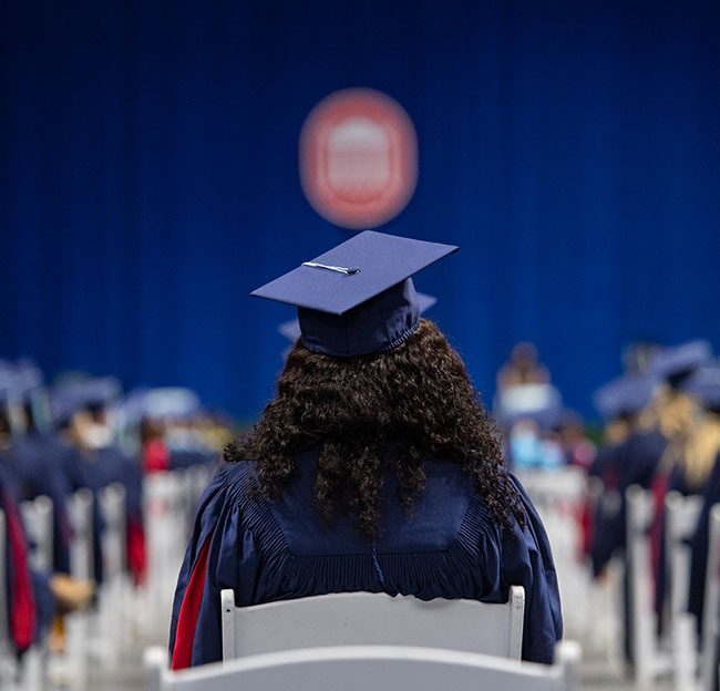 An Ole Miss student, in full graduation regalia, faces the stage at graduation in the Pavilion.